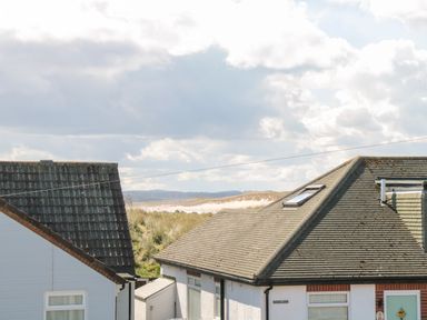 Roofs of two houses with grassy dunes and blue sky with clouds in the background at Dune View in Beadnell