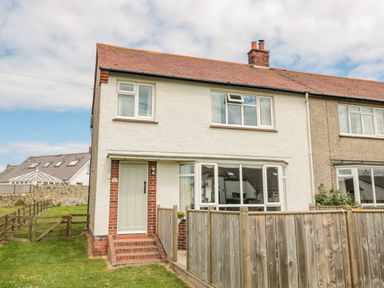 A semi detached house with a white front door and a wooden fence in the front garden at Dune View in Beadnell