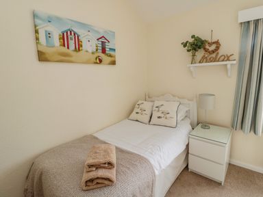 A bedroom with a single bed beside a nightstand with a lamp and a window at Dune View in Beadnell