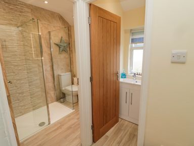 A bathroom with a glass shower enclosure a toilet and a sink with a cabinet at Dune View in Beadnell