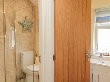 A bathroom with a toilet and glass shower enclosure next to a wooden door and a sink under a window at Dune View in Beadnell