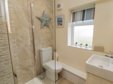 A bathroom with a toilet shower sink window with striped blind and three small plants on the sill at Dune View in Beadnell
