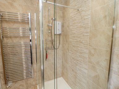 A shower area with glass doors chrome towel heater and beige tiled walls at Dune View in Beadnell