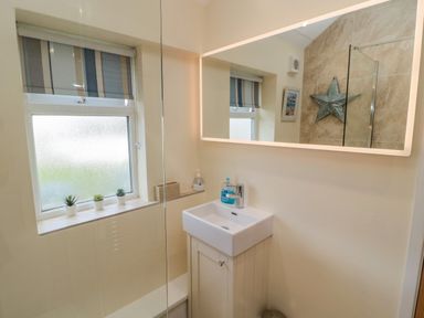 A bathroom with a sink cabinet small plants on the window and a large mirror at Dune View in Beadnell