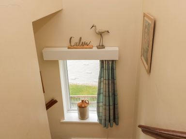 A staircase window with a decorative bird and calm sign above and a vase on the windowsill at Dune View in Beadnell