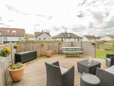 An outdoor wooden deck with black wicker furniture and a blue picnic table at Dune View in Beadnell