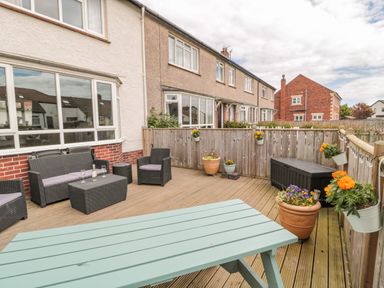 An outdoor patio with black wicker furniture a light blue picnic table and flower pots on the deck at Dune View in Beadnell