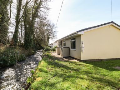 A yellow house next to a small flowing stream and grassy yard at 3 Rosecraddoc Lodge Rosecraddoc Lodge near Liskeard