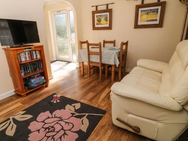 A living room with a cream sofa wooden dining table with chairs and a television on a wooden stand at 3 Rosecraddoc Lodge in Rosecraddoc Lodge near Liskeard