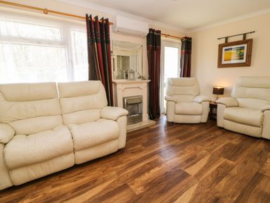 A living room with cream leather sofas a fireplace a mirror curtains a side table with a lamp and a framed picture on the wall at 3 Rosecraddoc Lodge Rosecraddoc Lodge near Liskeard