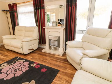 A living room with cream leather recliners a rug with floral pattern a fireplace and red and dark curtains at 3 Rosecraddoc Lodge near Liskeard