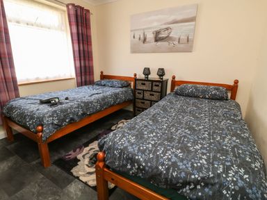 A bedroom with two single beds with floral bedspreads a bedside table with lamps and a window with plaid curtains at 3 Rosecraddoc Lodge Rosecraddoc Lodge near Liskeard
