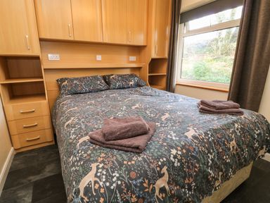 A bedroom with a double bed with patterned bedding and folded towels on top and wooden cabinets and shelves at 3 Rosecraddoc Lodge Rosecraddoc Lodge near Liskeard