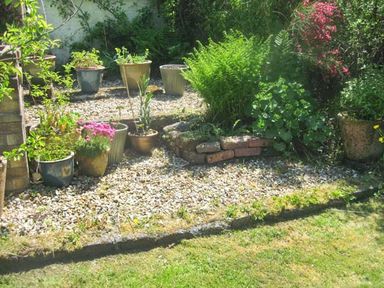 A gravel garden bed with multiple potted plants and shrubs next to a lawn at Lothlorien Cottage in Cwmgors near Ammanford