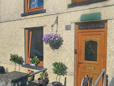 A house entrance with wooden door and windows with flower pots and hanging basket at Lothlorien Cottage in Cwmgors near Ammanford