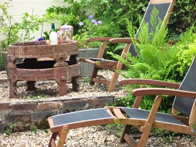A garden area with wooden lounge chairs and a carved wooden table surrounded by plants at Lothlorien Cottage in Cwmgors near Ammanford