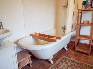 A bathroom with a clawfoot bathtub a wooden bath tray a wooden shelf a sink and a small wooden stool at Lothlorien Cottage in Cwmgors near Ammanford
