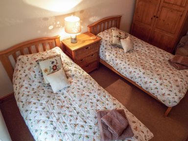 A bedroom with two single beds a wooden nightstand with a lamp and towels on one bed at Lothlorien Cottage in Cwmgors near Ammanford