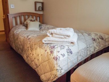 A bedroom with a single bed with floral quilt and pillows and folded towels on the bed at Lothlorien Cottage in Cwmgors near Ammanford