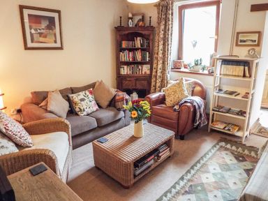 A living room with a sofa, armchairs, a coffee table with flowers, bookshelves, and a window at Lothlorien Cottage in Cwmgors near Ammanford