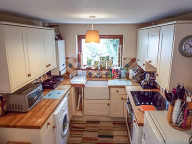 A kitchen with wooden countertops a washing machine a microwave a stove and a sink with plants on the windowsill at Lothlorien Cottage in Cwmgors near Ammanford