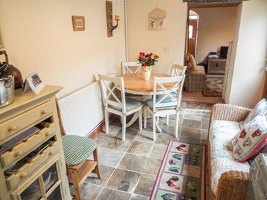 A dining area with a round table and four chairs a cabinet a chair and a sofa at Lothlorien Cottage in Cwmgors near Ammanford