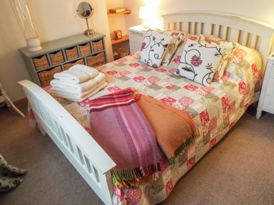 A bedroom with a white bed frame a patchwork quilt cushions folded towels and blankets beside a gray storage unit with baskets at Lothlorien Cottage in Cwmgors near Ammanford