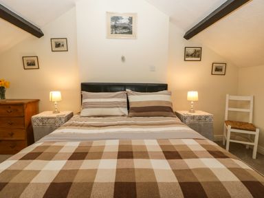 A bedroom with a double bed with striped bedding two bedside tables with lamps a wooden chest of drawers and a chair at The Coach House in Gilwern near Crickhowell and Abergavenny