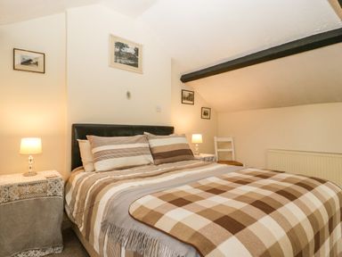 A bedroom with a double bed striped bedding and a checkered blanket two bedside tables with lamps a white chair and framed pictures on the walls at The Coach House in Gilwern near Crickhowell and Abergavenny