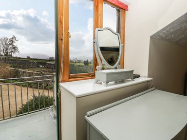 A room with a desk and a small mirror on a cabinet by a window showing an outside view at The Coach House in Gilwern near Crickhowell and Abergavenny
