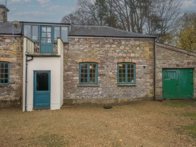 A stone building with green doors and windows and a gravel yard at The Coach House in Gilwern near Crickhowell and Abergavenny