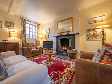 A living room with two armchairs a sofa a fireplace with a fire a red patterned rug and a wooden table at The Coach House in Gilwern near Crickhowell and Abergavenny