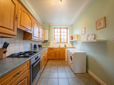 A kitchen with wooden cabinets a gas stove an oven a washing machine and a window at The Coach House in Gilwern near Crickhowell and Abergavenny