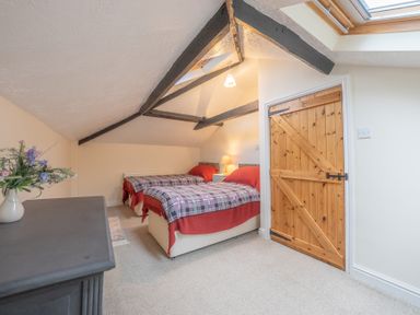 A bedroom with two single beds side by side with checkered blankets and a wooden door at The Coach House in Gilwern near Crickhowell and Abergavenny