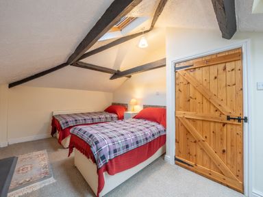 A bedroom with two single beds under a sloped ceiling with exposed wooden beams at The Coach House in Gilwern near Crickhowell and Abergavenny