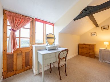 A room with a wooden door with a tied curtain a white desk with mirror a wooden chair a wooden chest of drawers and a table with a lamp at The Coach House in Gilwern near Crickhowell and Abergavenny