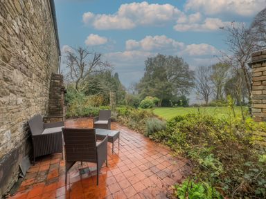 An outdoor patio with wet red tiles and brown chairs next to a stone wall with greenery and trees in the background at The Coach House Gilwern near Crickhowell and Abergavenny