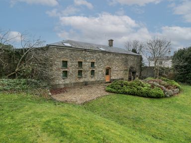 A stone building with small windows a wooden door a garden with bushes and grass at The Coach House in Gilwern near Crickhowell and Abergavenny