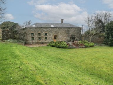 An exterior view of a stone building with small windows and a door in a grassy garden at The Coach House in Gilwern near Crickhowell and Abergavenny