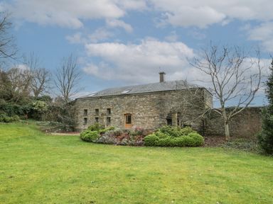 A stone building with small windows and a wooden door surrounded by grass and bushes at The Coach House in Gilwern near Crickhowell and Abergavenny