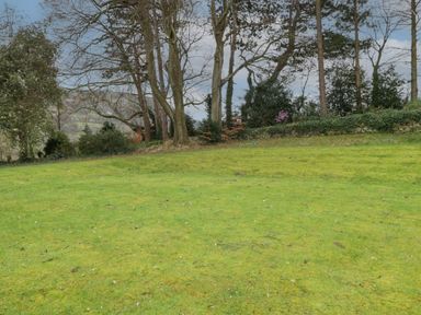 A grassy lawn with trees and shrubs in the background at The Coach House in Gilwern near Crickhowell and Abergavenny