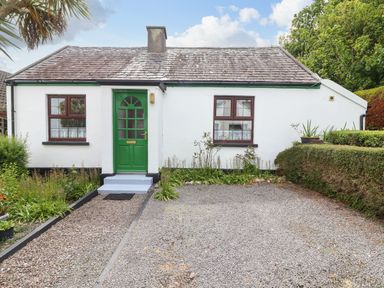 A white cottage with green door and windows surrounded by gravel driveway and trimmed bushes at Brendans Cottage in Valentia Island County Kerry