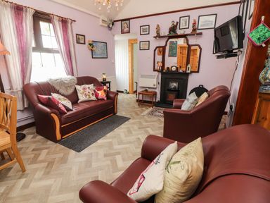 A living room with maroon leather sofas, floral cushions, a fireplace, a wall-mounted TV, and decorative items at Brendan's Cottage in Valentia Island County Kerry