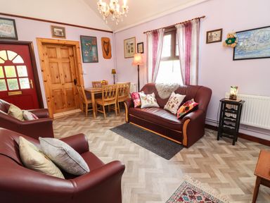 A sitting room with brown leather sofas a wooden dining table wooden door and framed pictures on the walls at Brendan's Cottage Valentia Island County Kerry