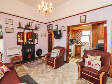 A living room with two leather armchairs a sofa and a fireplace leading to a kitchen at Brendans Cottage Valentia Island County Kerry