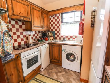 A kitchen with wooden cabinets a white oven dishwasher and washing machine a window above the sink and red and white checkered tiles at Brendans Cottage in Valentia Island County Kerry