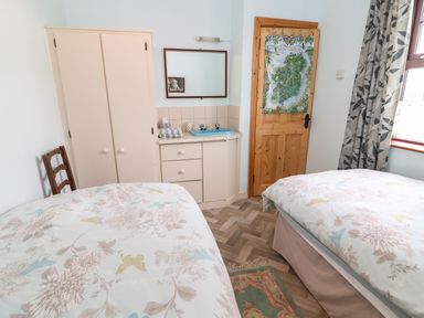 A bedroom with two beds a wooden chair a wardrobe a sink with a mirror and a door with a map at Brendans Cottage Valentia Island County Kerry