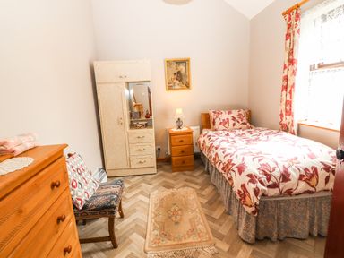 A bedroom with a single bed next to a window a wardrobe a wooden chair a chest of drawers and a small rug on the floor at Brendan's Cottage Valentia Island County Kerry