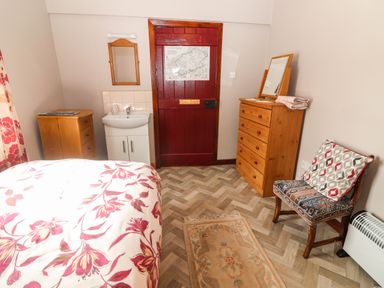 A bedroom with a bed with floral bedding a wooden dresser a chair with a cushion a small rug and a sink at Brendan's Cottage in Valentia Island County Kerry