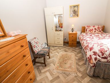 A bedroom with a single bed table lamp wooden chest of drawers chair and a small rug at Brendans Cottage Valentia Island County Kerry